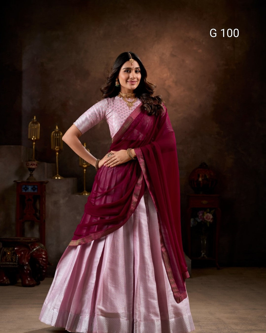 Woman wearing a pink saree with a maroon border in a studio setting