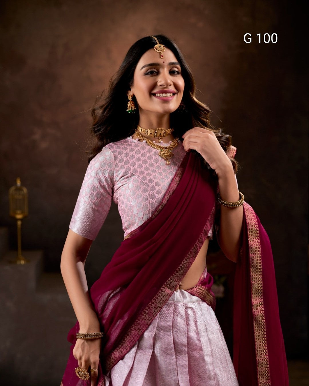 Woman in traditional attire with a maroon saree and pink blouse against a dark background