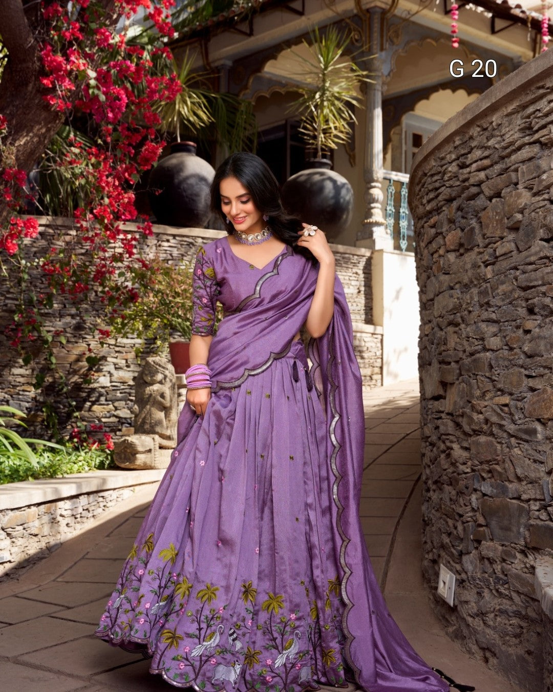 Woman in a purple saree standing outdoors with decorative elements.