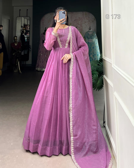 Person wearing a long purple dress with white embroidery in a room.