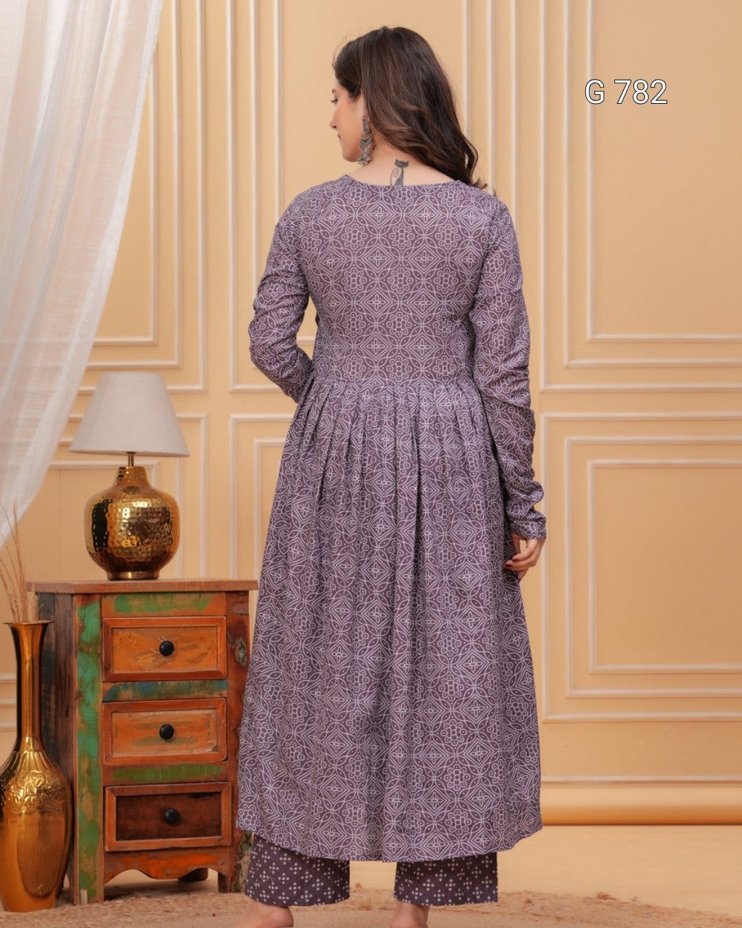 Woman wearing a long, patterned dress in a room with wooden furniture and decorative elements.
