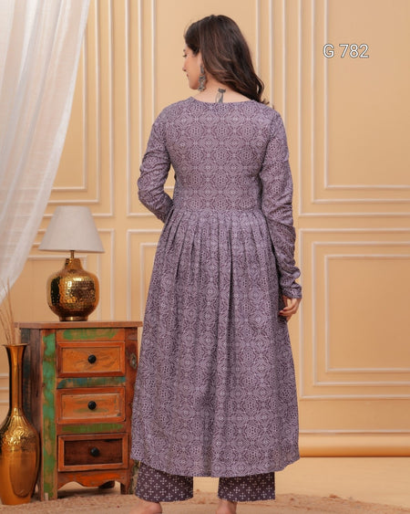 Woman wearing a long, patterned dress in a room with wooden furniture and decorative elements.