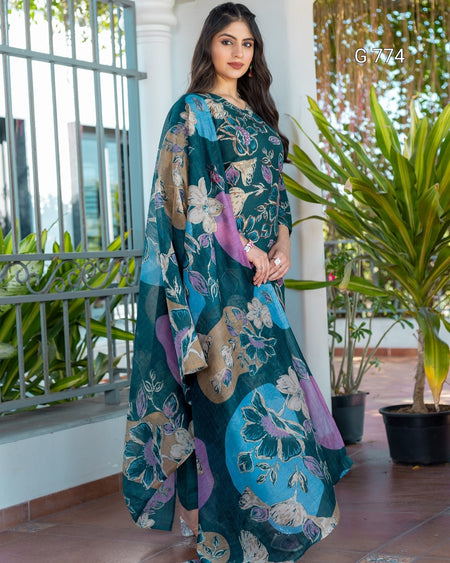 Woman wearing a teal floral saree with a background of plants and a railing.