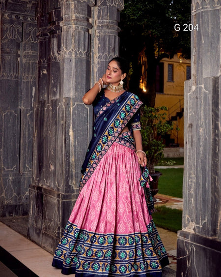Woman in a traditional pink and blue saree standing in front of stone pillars.