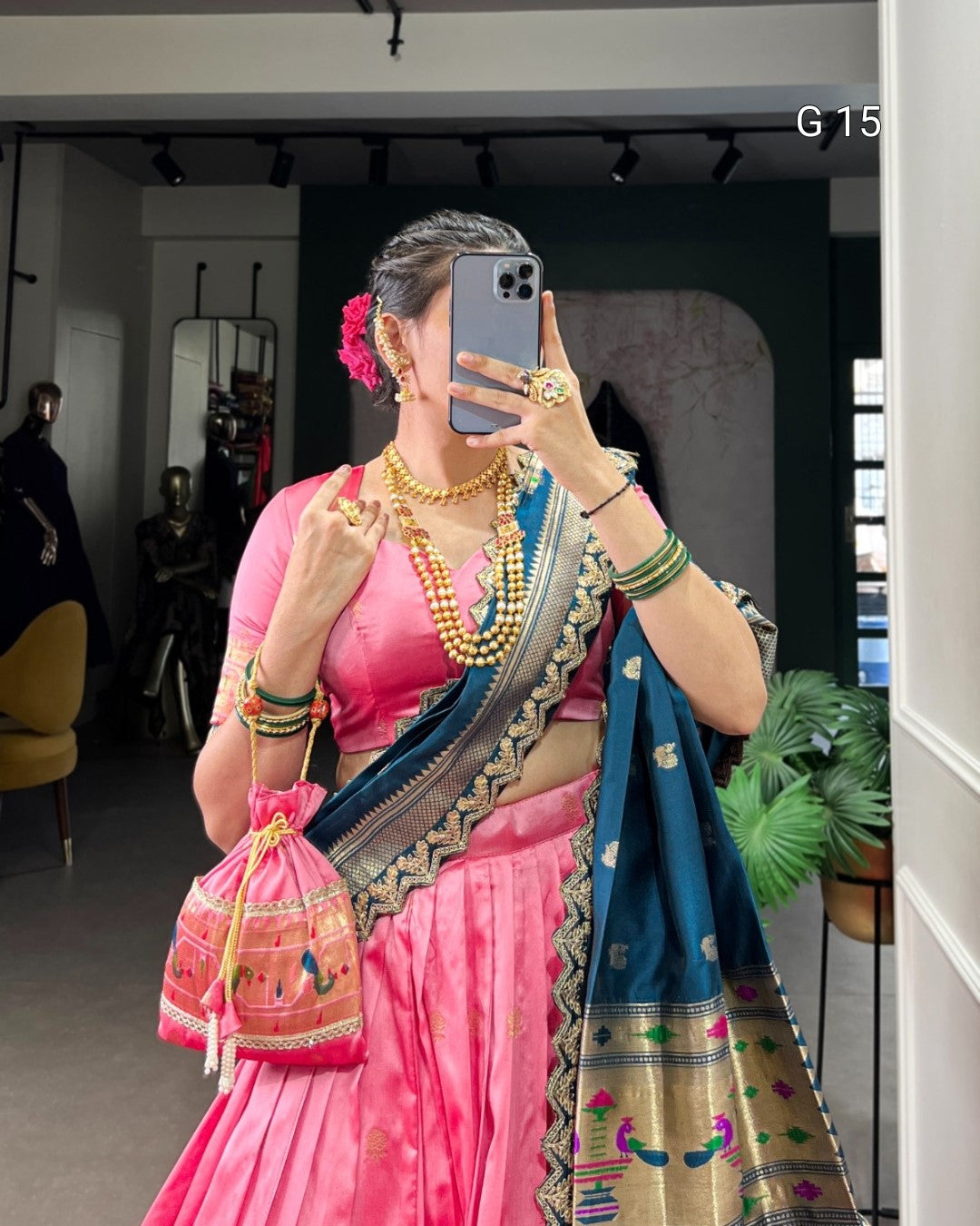 Person wearing a pink and blue saree with jewelry, taking a mirror selfie.