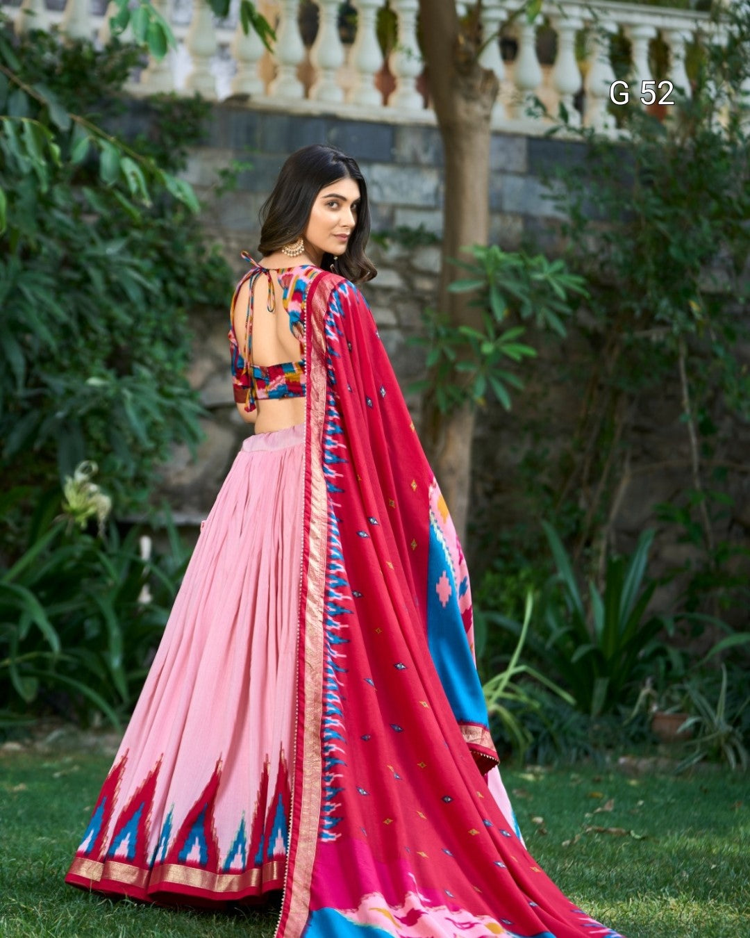 Woman in a colorful traditional outfit with a pink skirt and blue dupatta standing outdoors.
