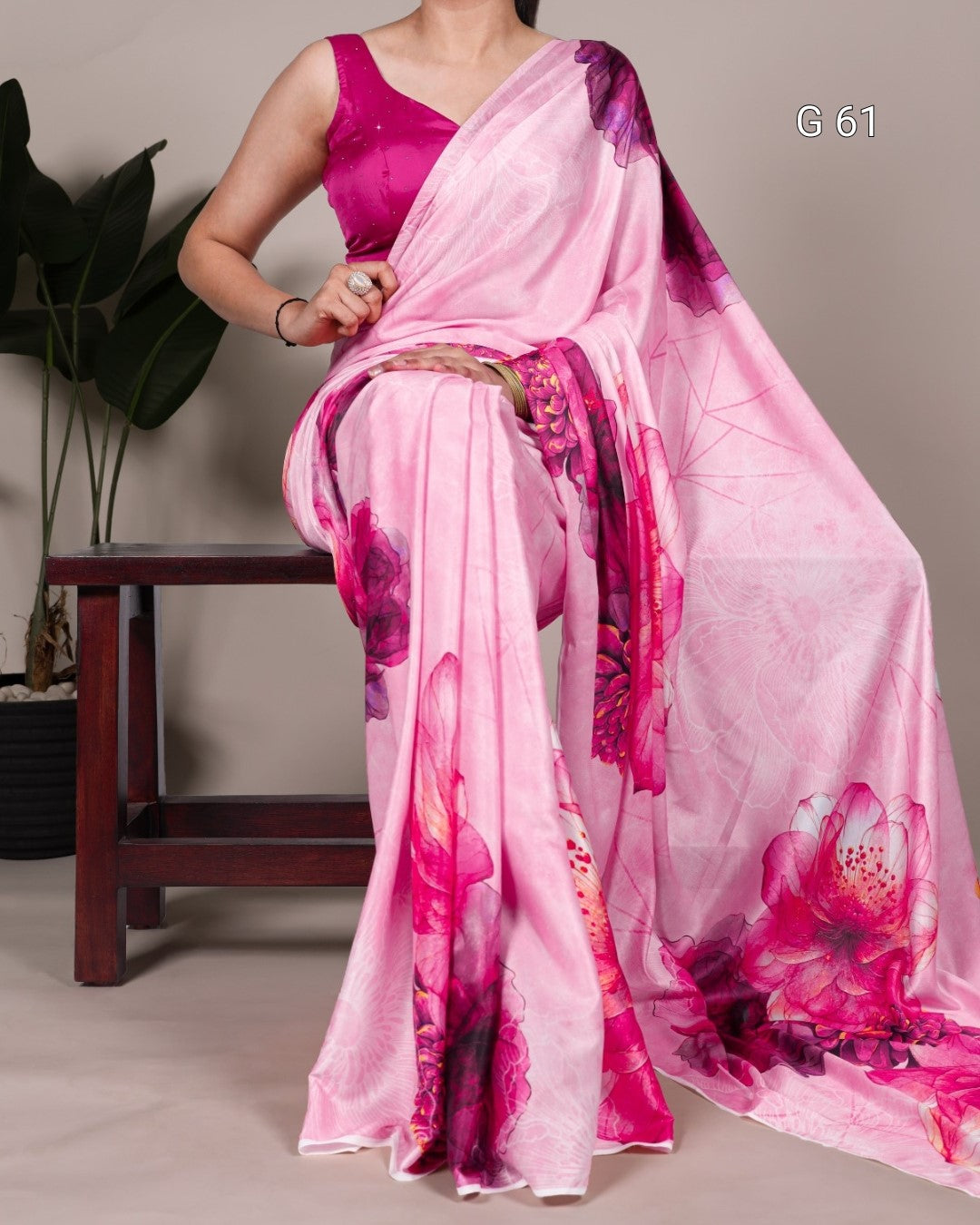 Woman wearing a pink saree with floral patterns, sitting on a chair.