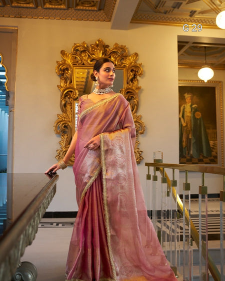 Woman in a pink saree standing in a decorated interior setting with a large mirror.