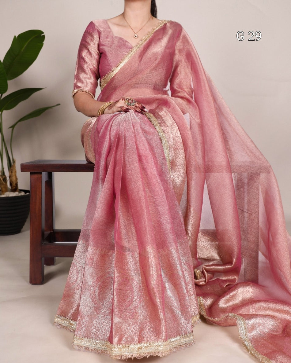 Person wearing a pink saree with gold border sitting on a chair.