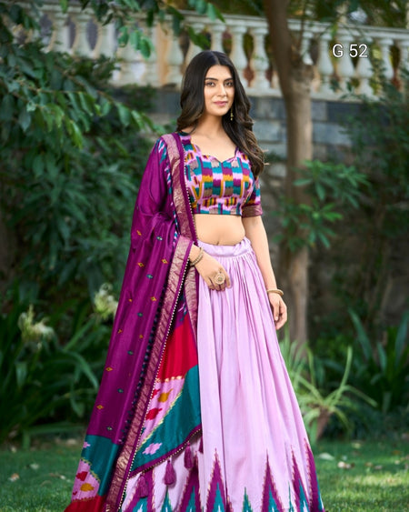 Woman in a colorful traditional outfit standing outdoors with greenery in the background