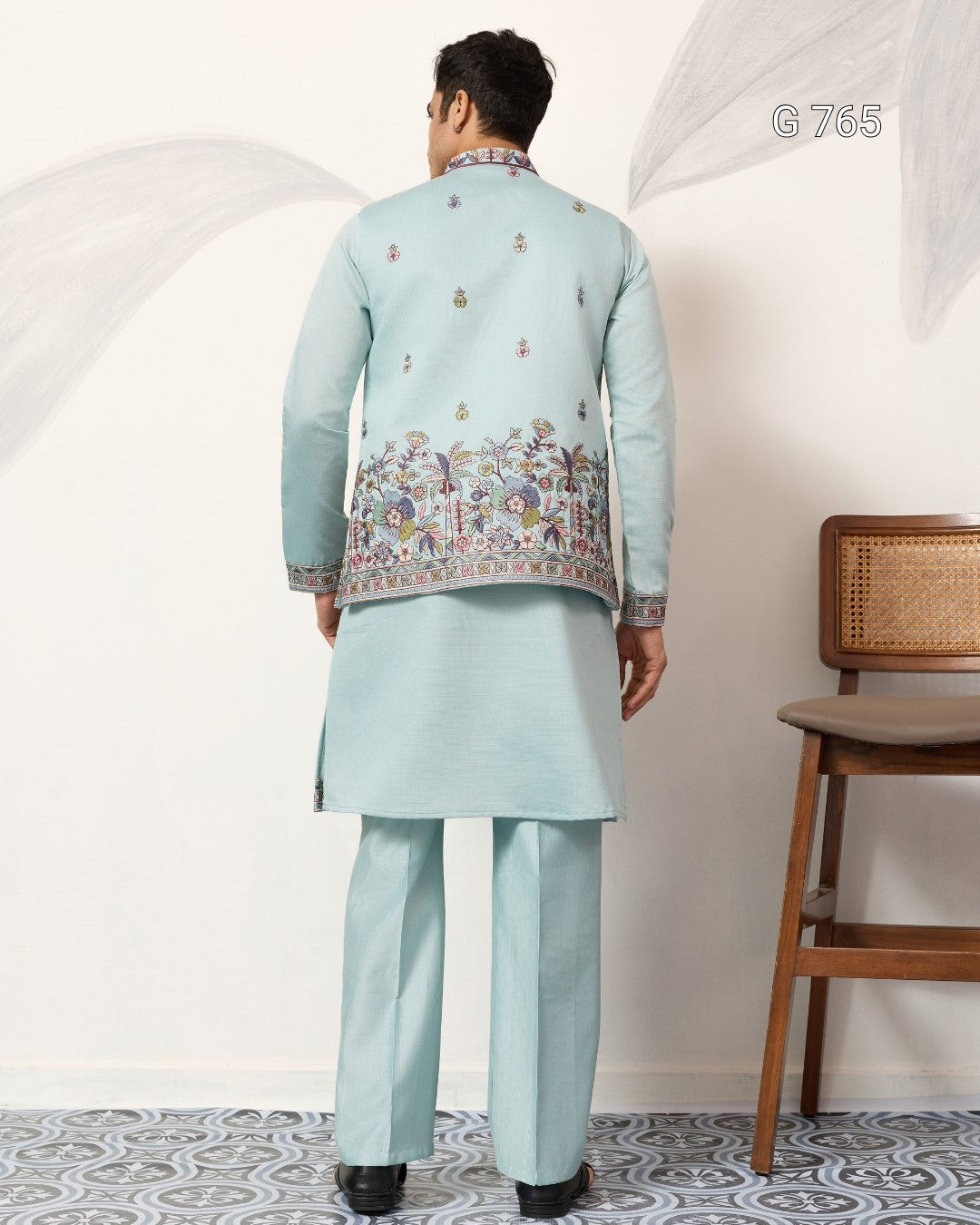 Man wearing a light blue embroidered traditional outfit in a minimalistic room.