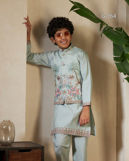 Child wearing a light blue embroidered traditional outfit standing against a beige wall with a plant.