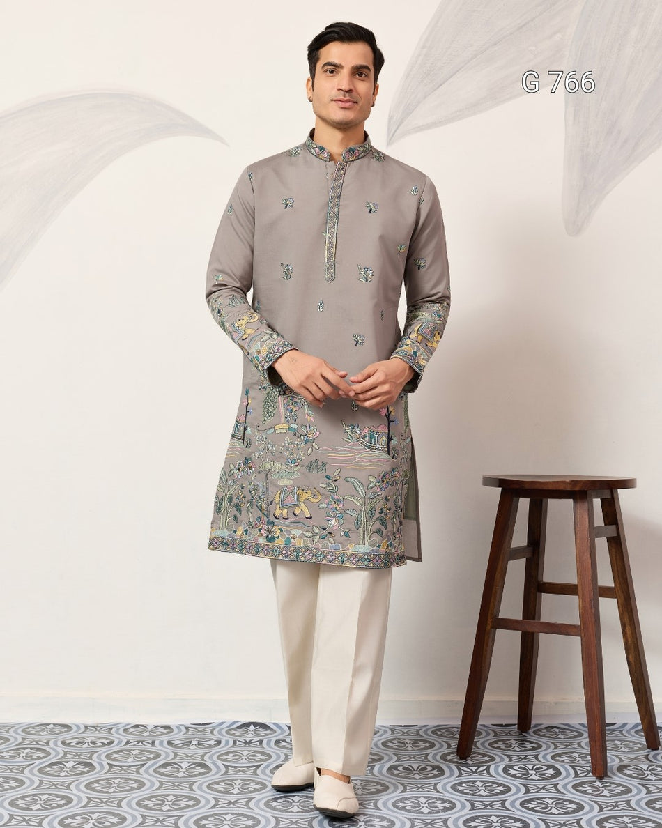 Man wearing a gray kurta with white pants standing in a room with a wooden stool.