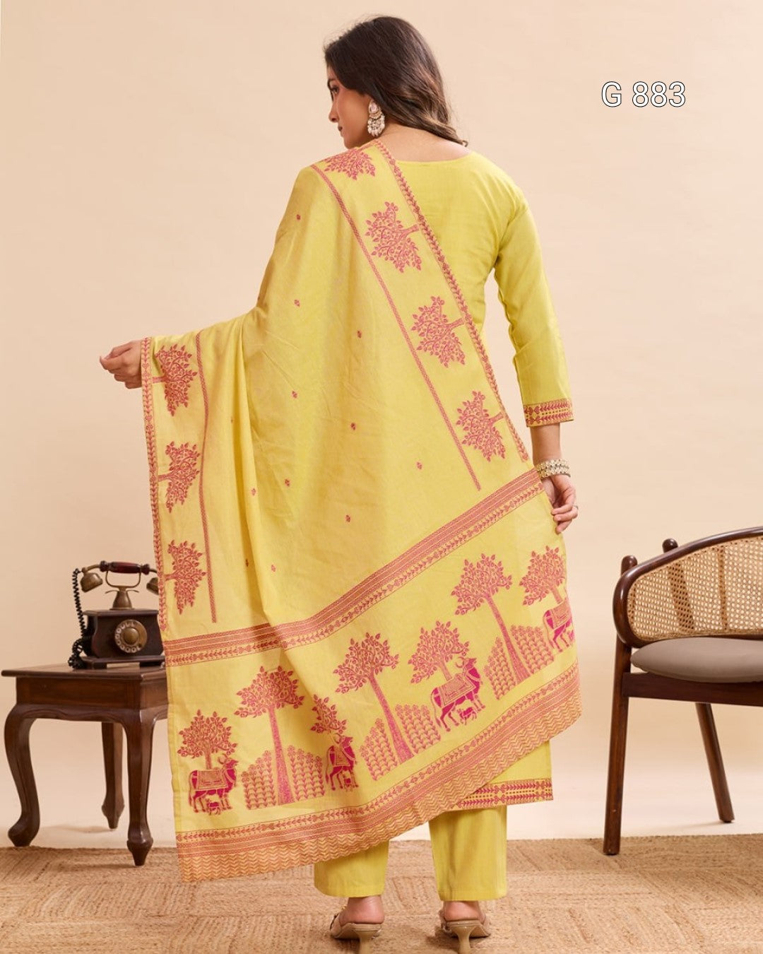Woman wearing a yellow traditional outfit with pink embroidery in a room setting.