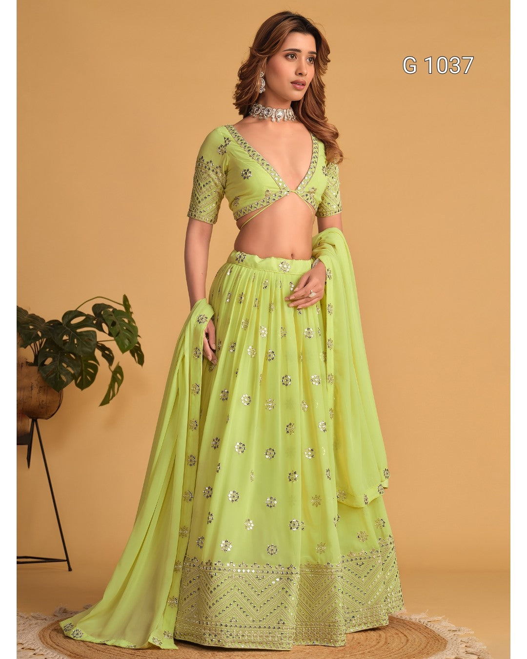 A woman models a light lime green traditional Indian lehenga choli set with silver mirror work embroidery, set against a solid beige background.
