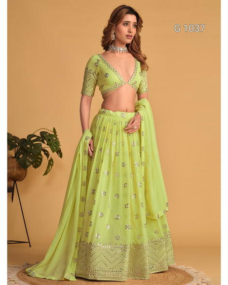 A woman models a light lime green traditional Indian lehenga choli set with silver mirror work embroidery, set against a solid beige background.
