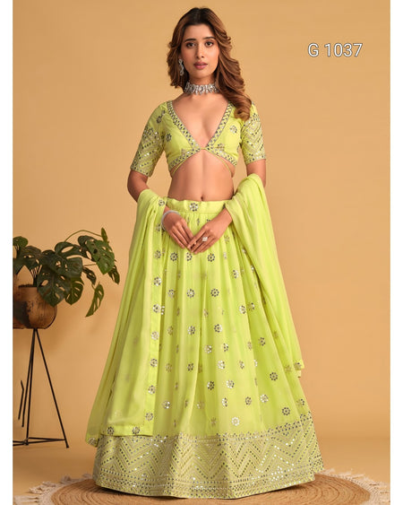 A woman models a light lime green traditional Indian lehenga choli set with silver mirror work embroidery, set against a solid beige background.