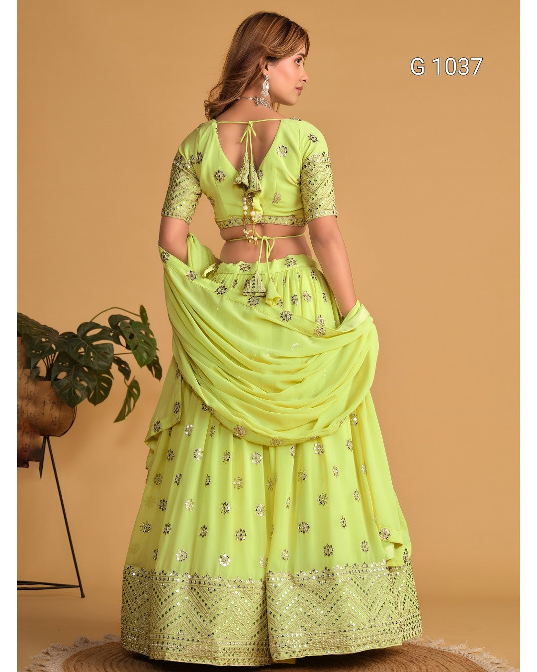 A woman modeling a light lime green traditional Indian lehenga choli set with silver floral embroidery, shown from the back against a warm beige background.