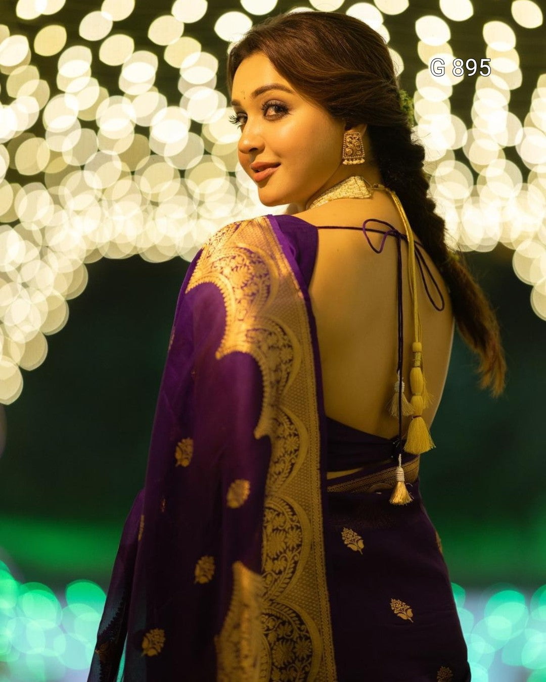 Woman in a purple and gold saree with a blurred bokeh background