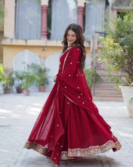 Woman in a red saree with gold details standing outdoors.