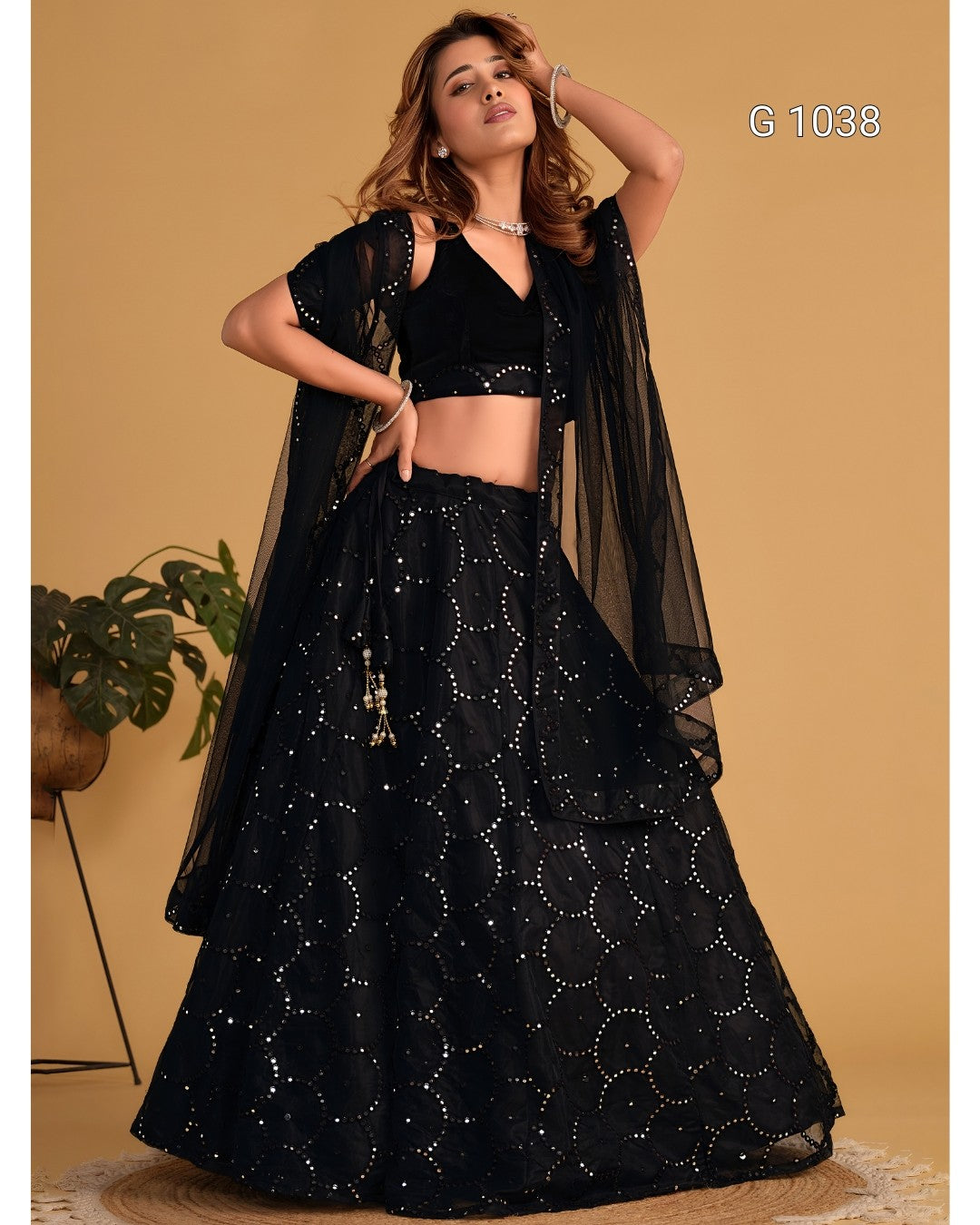 A woman modeling a black embroidered Indian ethnic outfit with a flared skirt, cropped black top, and sheer black draped overlay against a warm beige studio background. White text in the top right reads 'G 1038'.