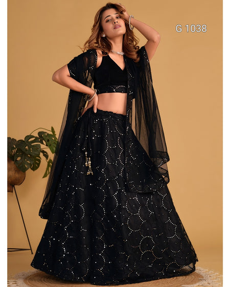 A woman modeling a black embroidered Indian ethnic outfit with a flared skirt, cropped black top, and sheer black draped overlay against a warm beige studio background. White text in the top right reads 'G 1038'.