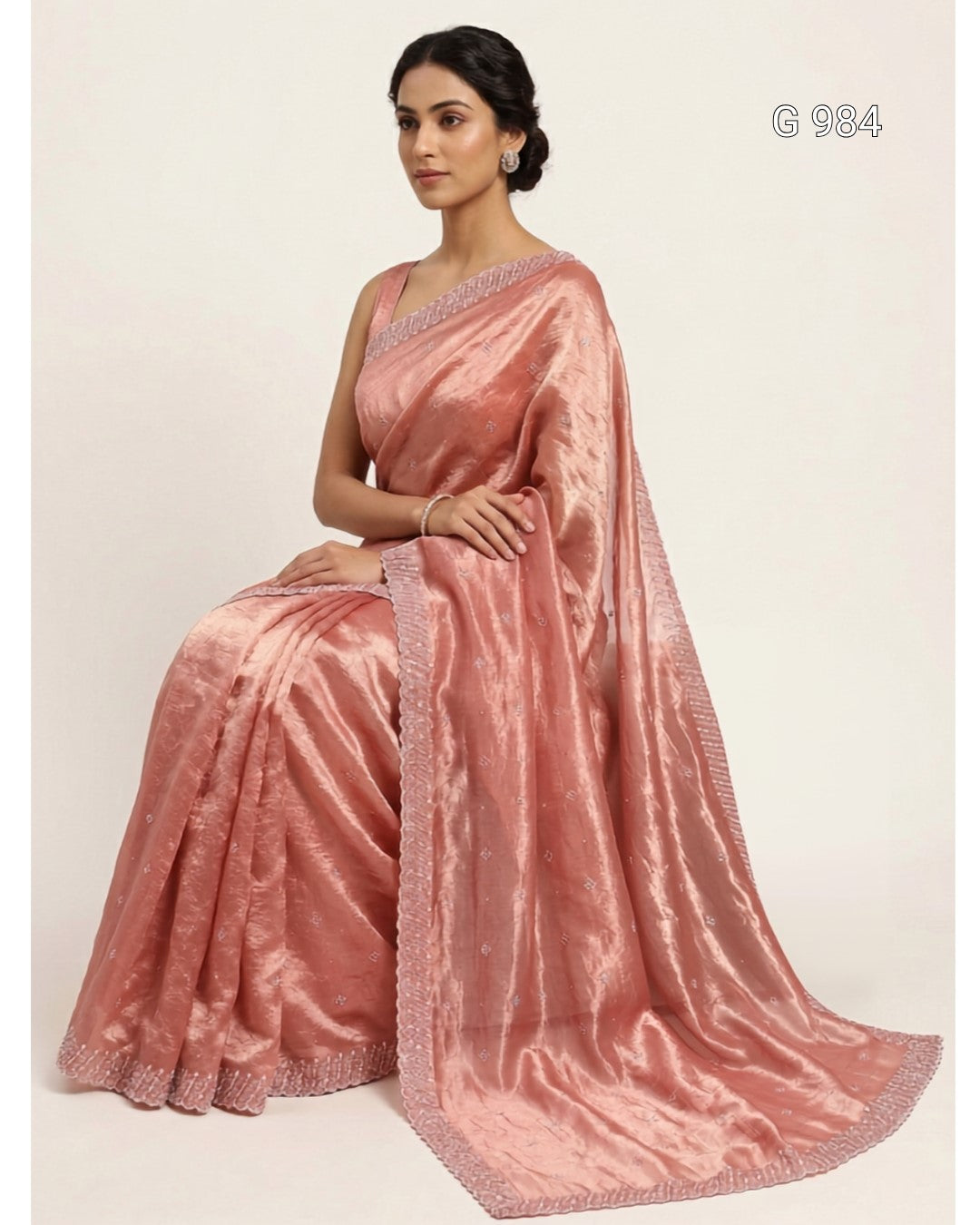 A woman seated and wearing a shimmering pink satin saree with a matching draped pallu and embroidered border, photographed against a plain light beige studio background. The code 'G 984' appears in the top right.