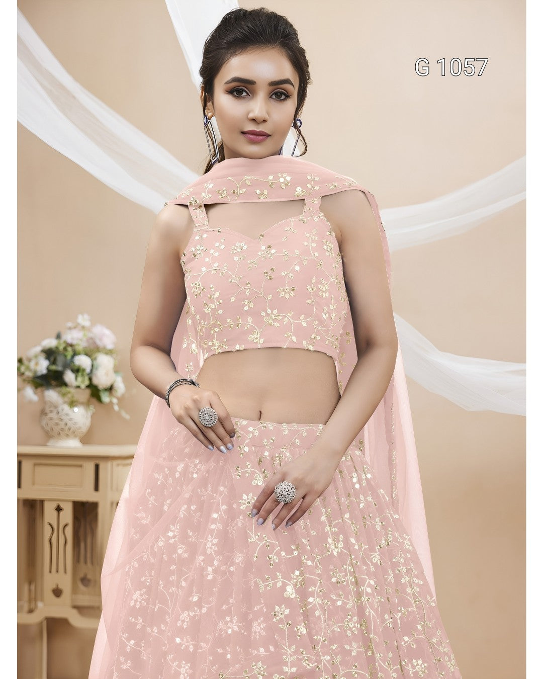 A woman modeling a light pink traditional Indian ethnic wear set with gold floral embroidery, featuring a sleeveless crop top, flared skirt, and matching dupatta.