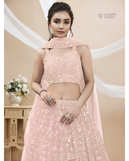 A woman modeling a light pink traditional Indian ethnic wear set with gold floral embroidery, featuring a sleeveless crop top, flared skirt, and matching dupatta.