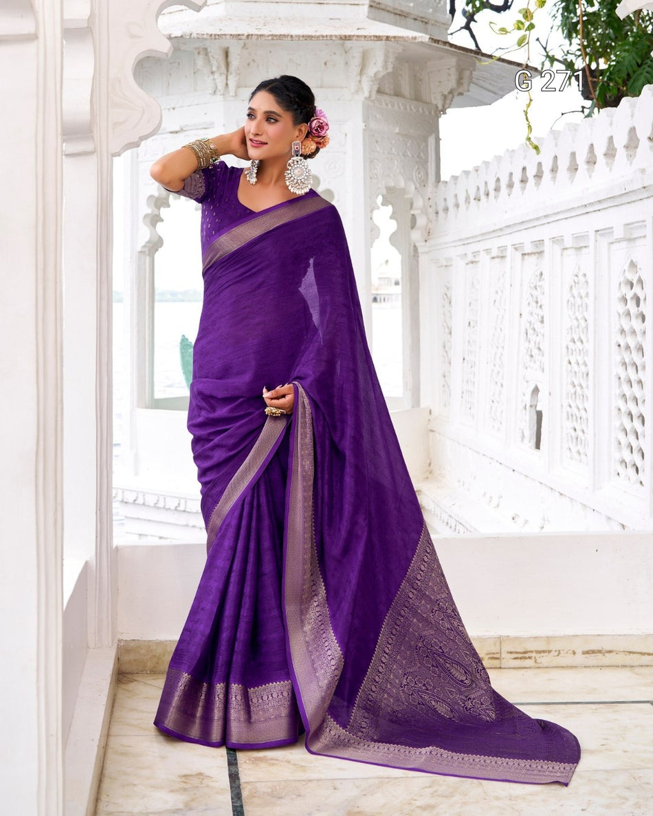 A woman models a purple silk saree with a metallic silver border and pallu, standing in a white architectural corridor.