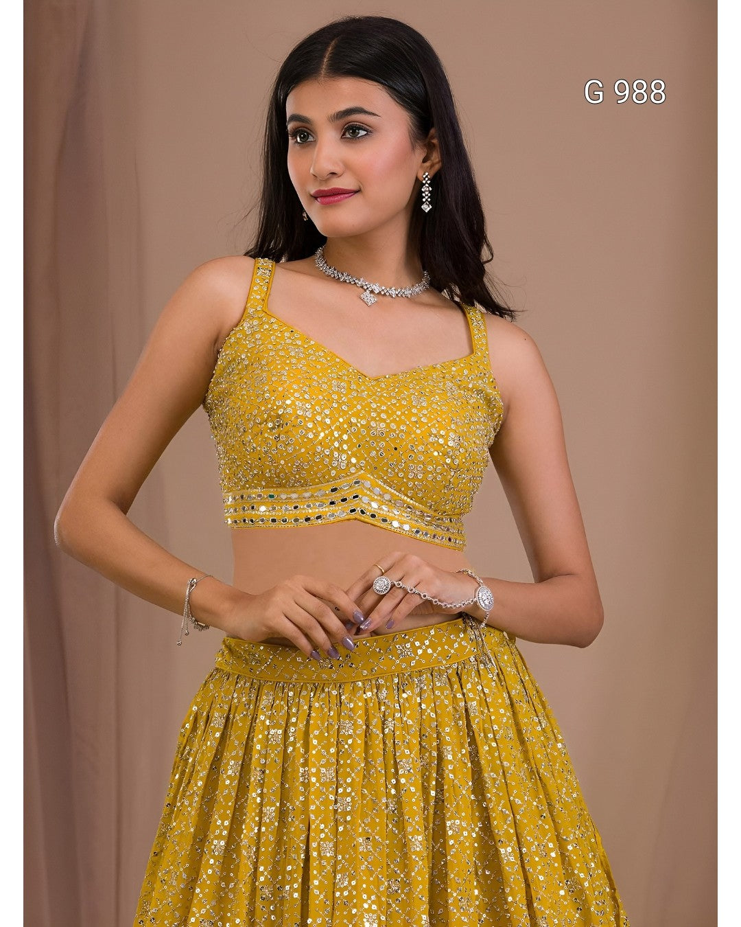 A woman modeling a yellow embellished two-piece traditional outfit with a sleeveless crop top and flared skirt, photographed against a plain beige backdrop. The text 'G 988' appears in the top right.