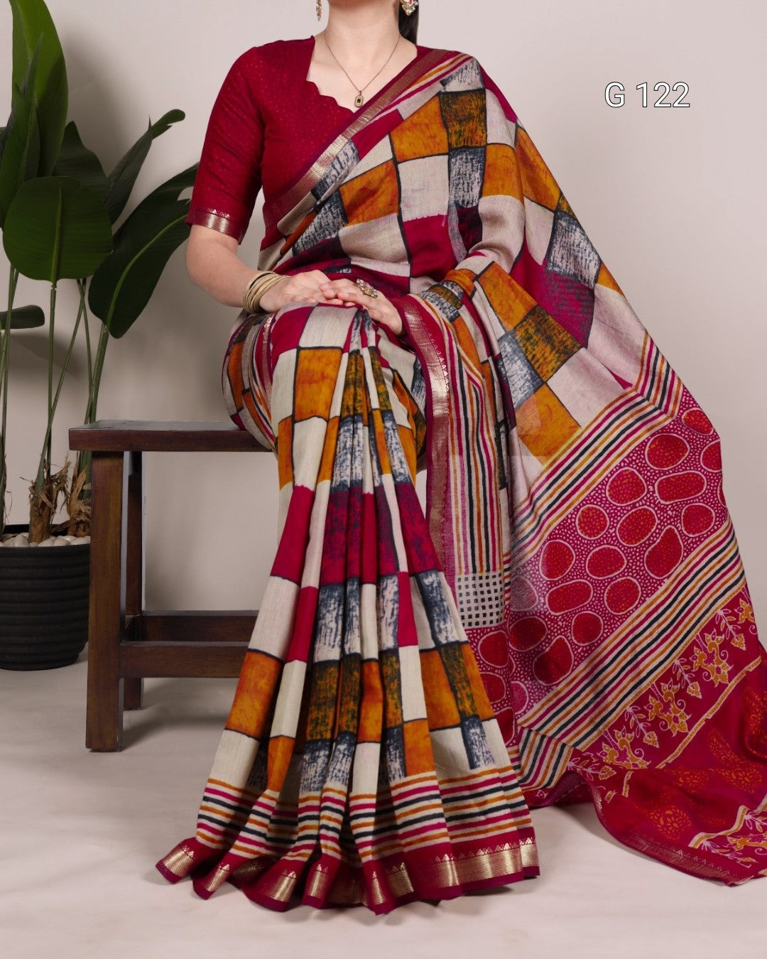Woman wearing a colorful saree with a patterned design, sitting on a wooden stool.
