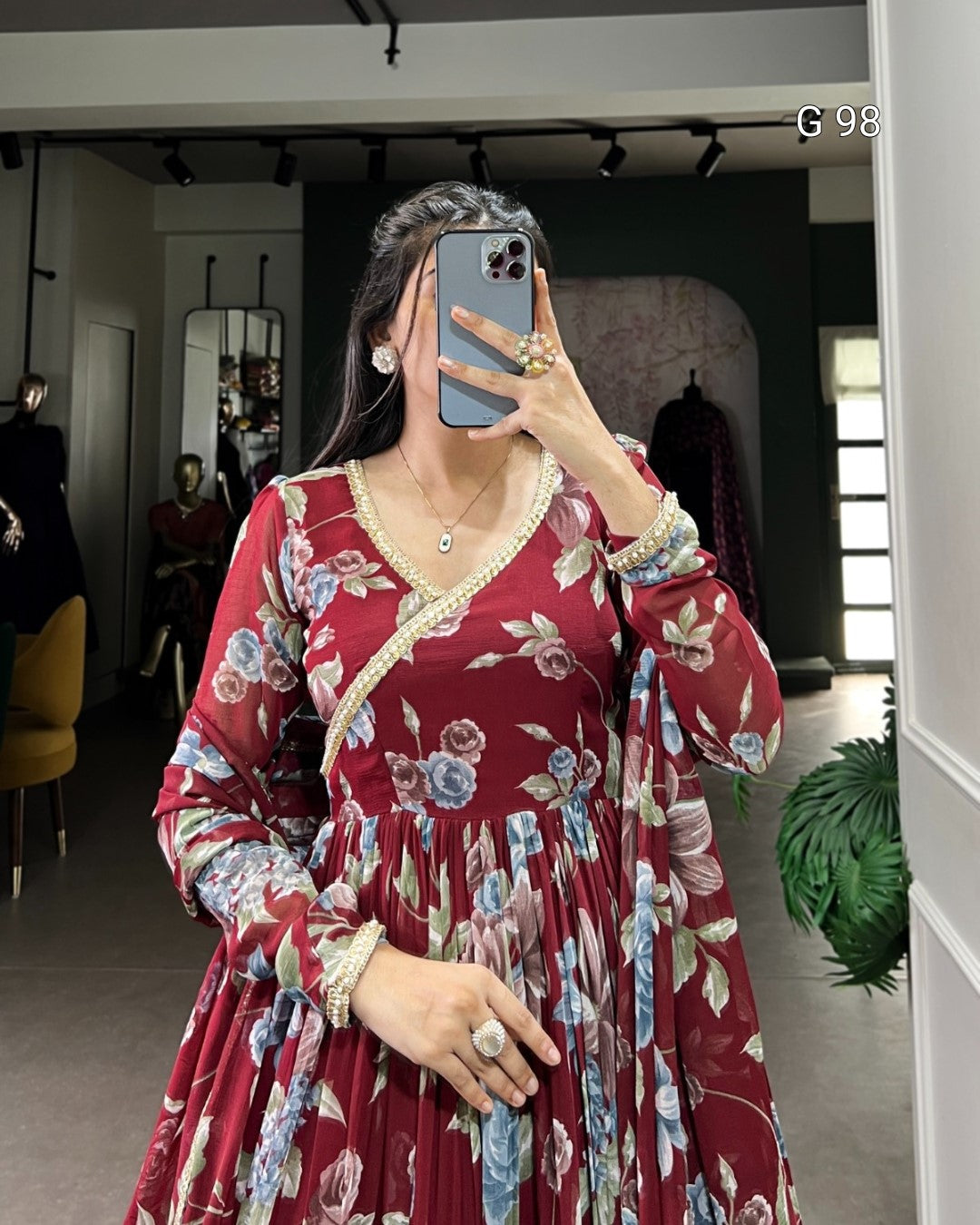 Woman taking a mirror selfie wearing a red floral dress in an indoor setting.