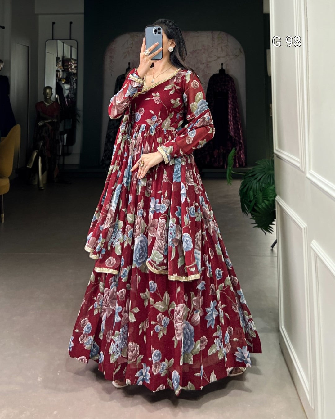 Woman wearing a long, floral-patterned dress taking a mirror selfie.