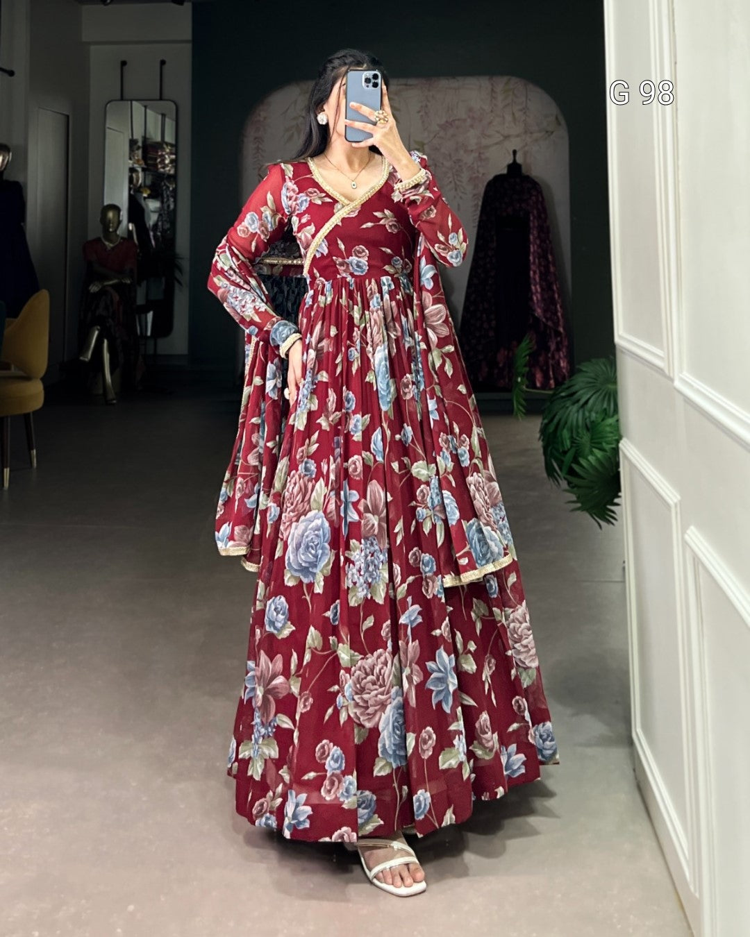 Woman wearing a red floral dress taking a mirror selfie in a room.