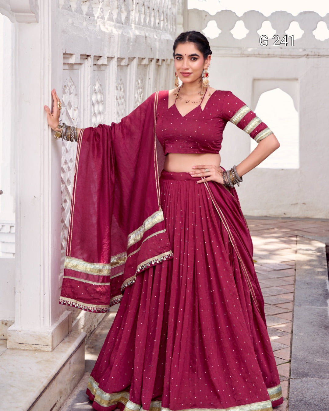 Woman wearing a maroon traditional outfit with gold accents in a white architectural setting