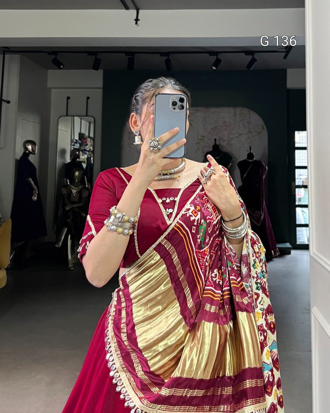 Woman taking a mirror selfie wearing a traditional maroon and gold saree with a colorful blouse.