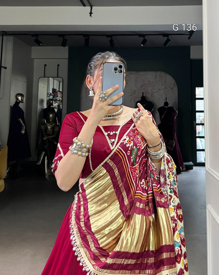 Woman taking a mirror selfie wearing a traditional maroon and gold saree with a colorful blouse.