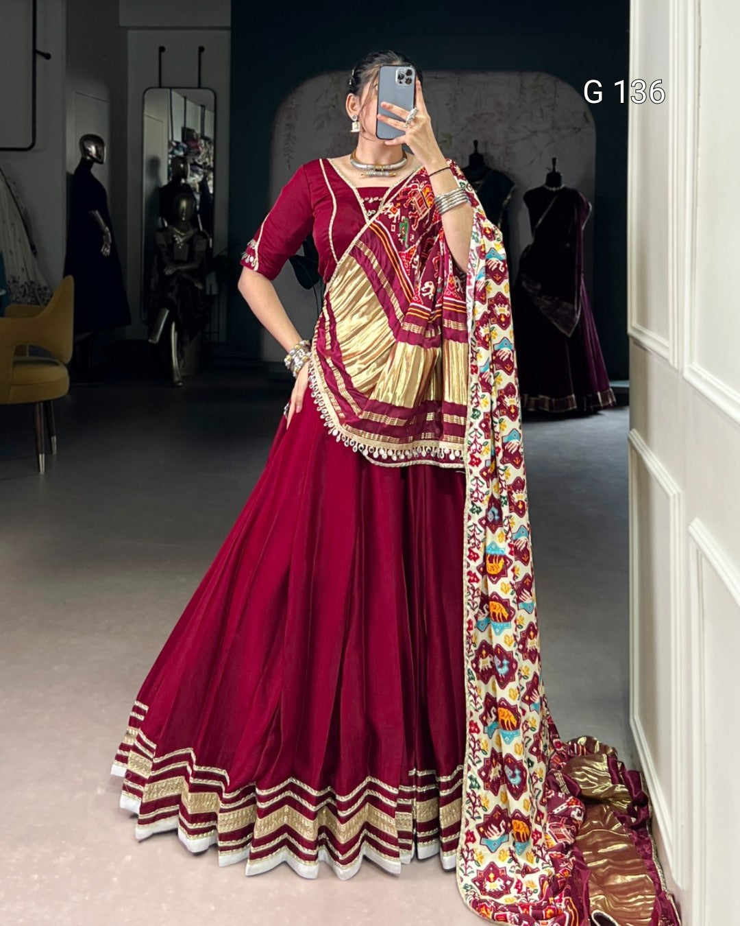 Person wearing a red saree with gold border and colorful dupatta in a room.