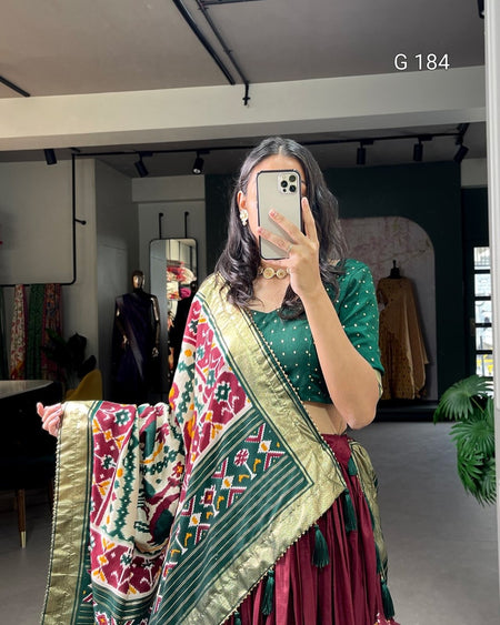 Woman taking a mirror selfie wearing a green saree with a colorful border in an indoor setting.