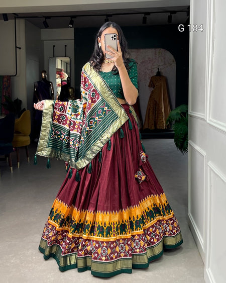 Woman wearing a traditional maroon and green saree with a colorful border, taking a mirror selfie.