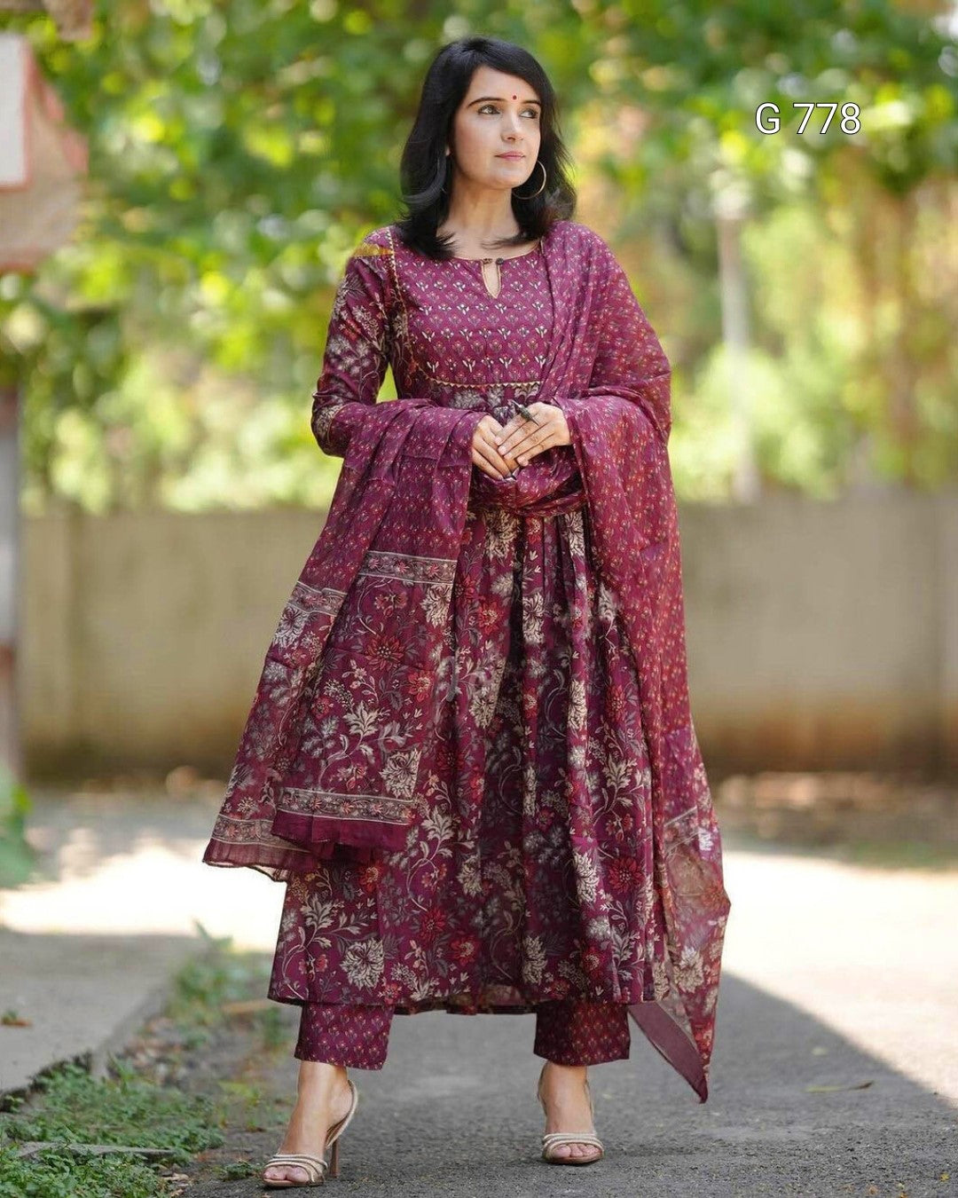 Woman wearing a traditional maroon and pink outfit with a floral pattern outdoors.