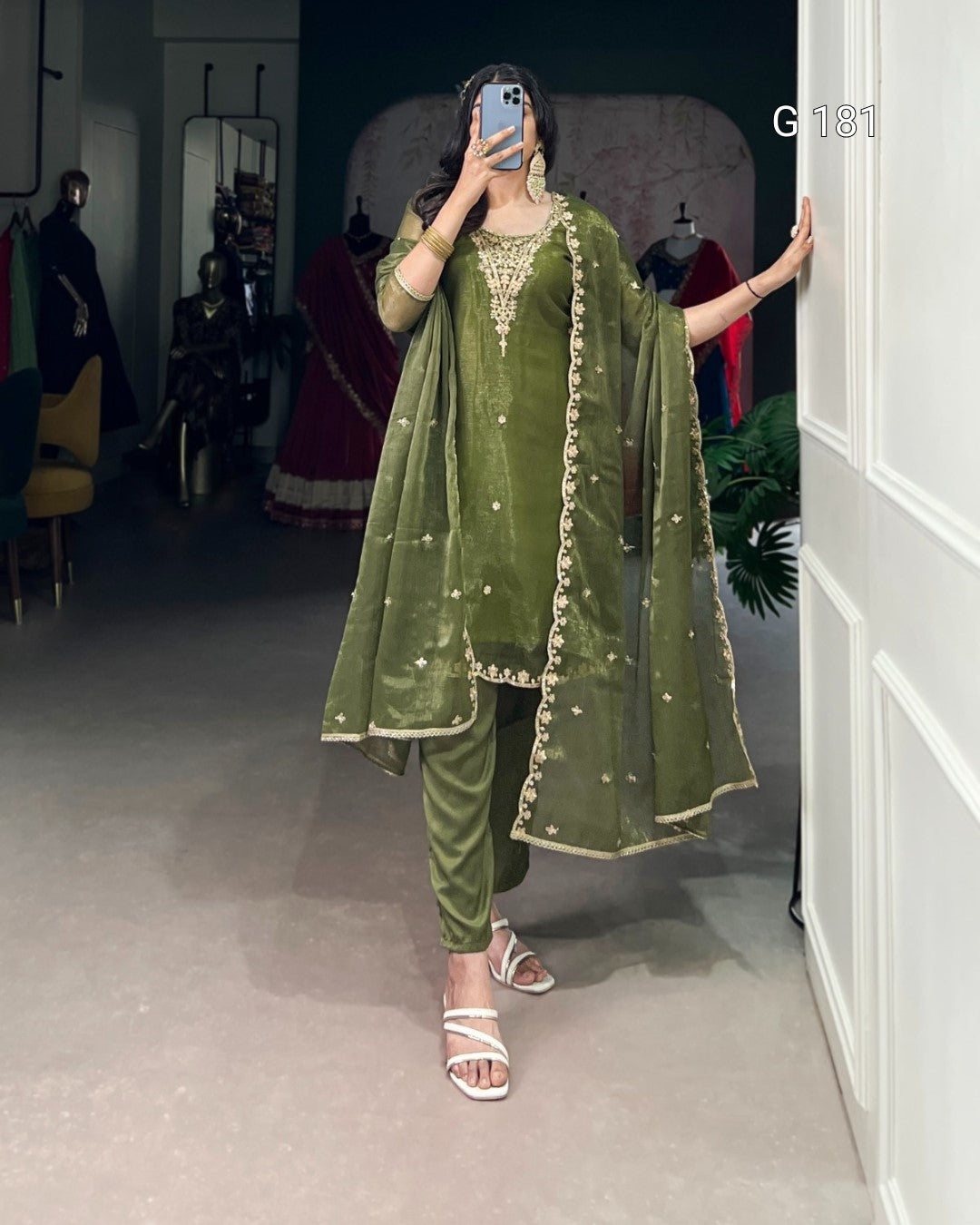 Person wearing a green traditional outfit with gold details in a room setting.