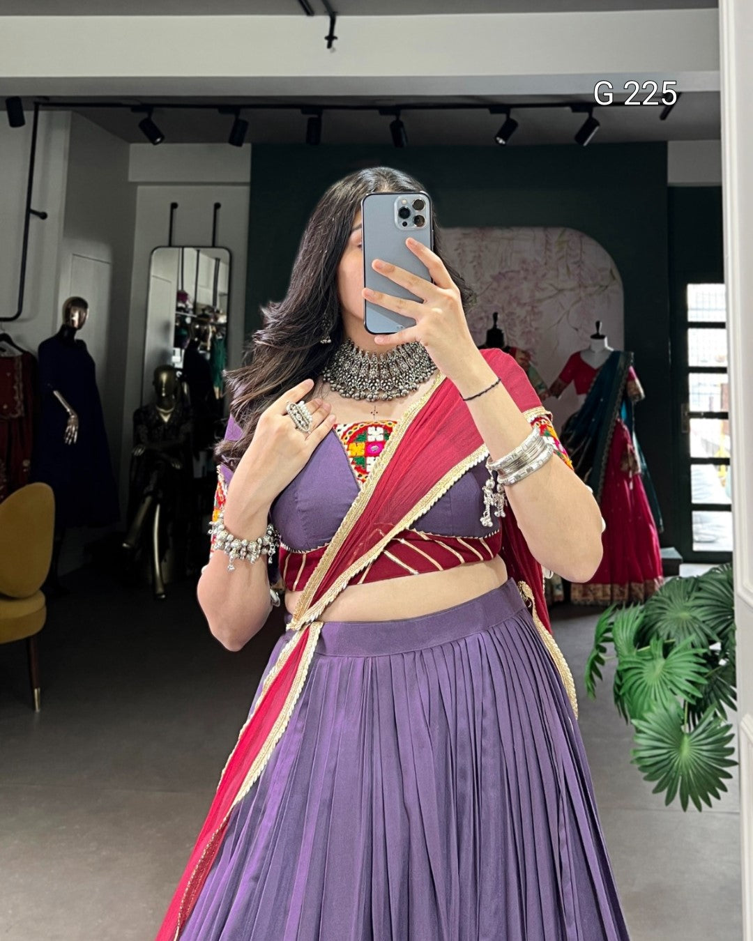 Woman taking a mirror selfie wearing a traditional outfit with a purple saree and red blouse in a store setting.
