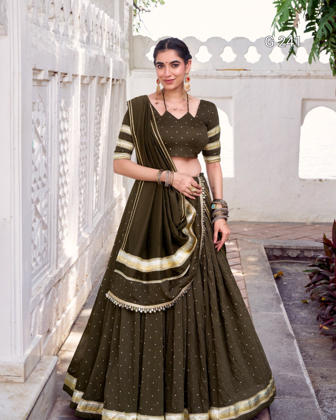 Woman in a traditional dark green saree with gold accents standing in a decorative outdoor setting.