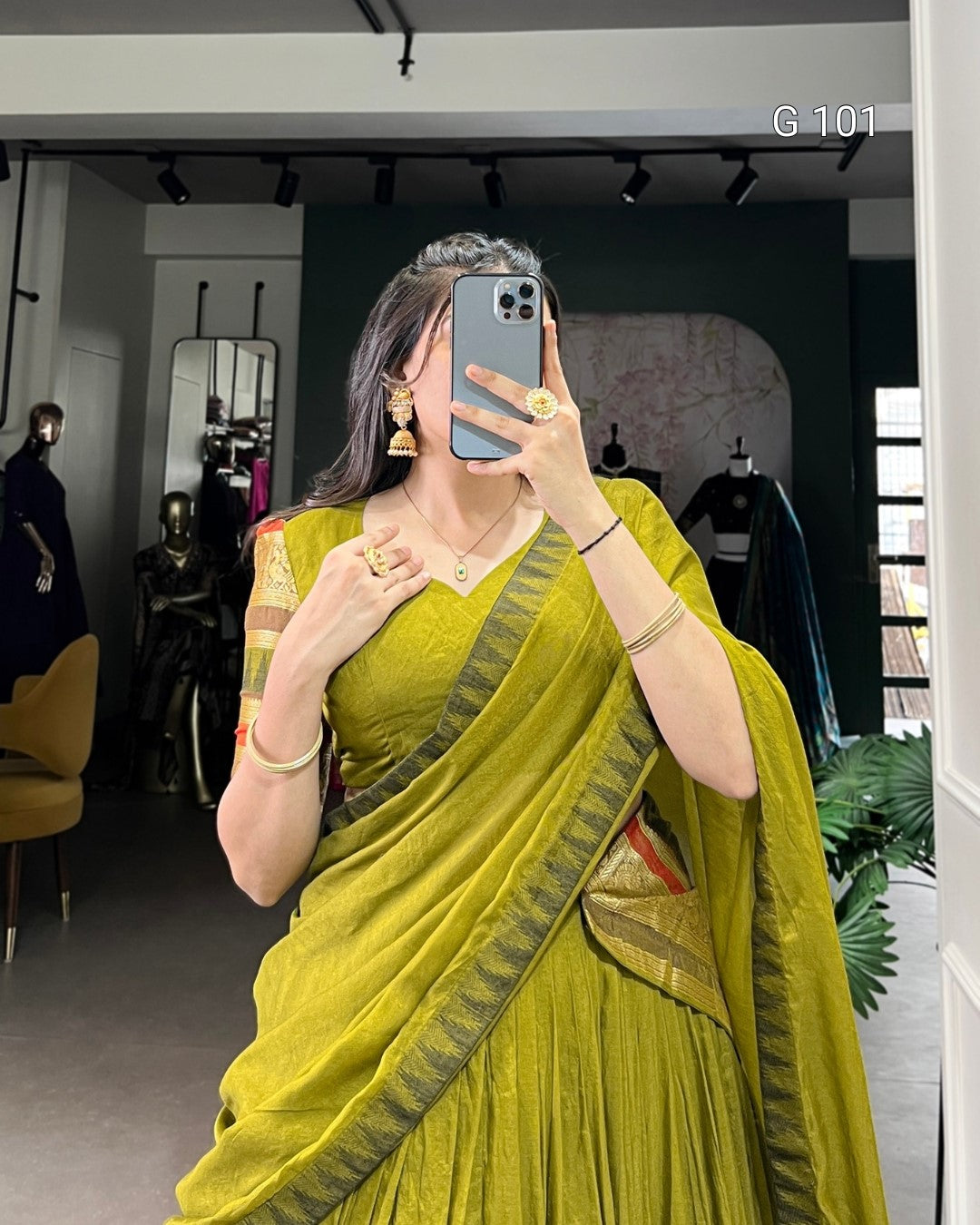 Woman in a green saree taking a mirror selfie in a store.