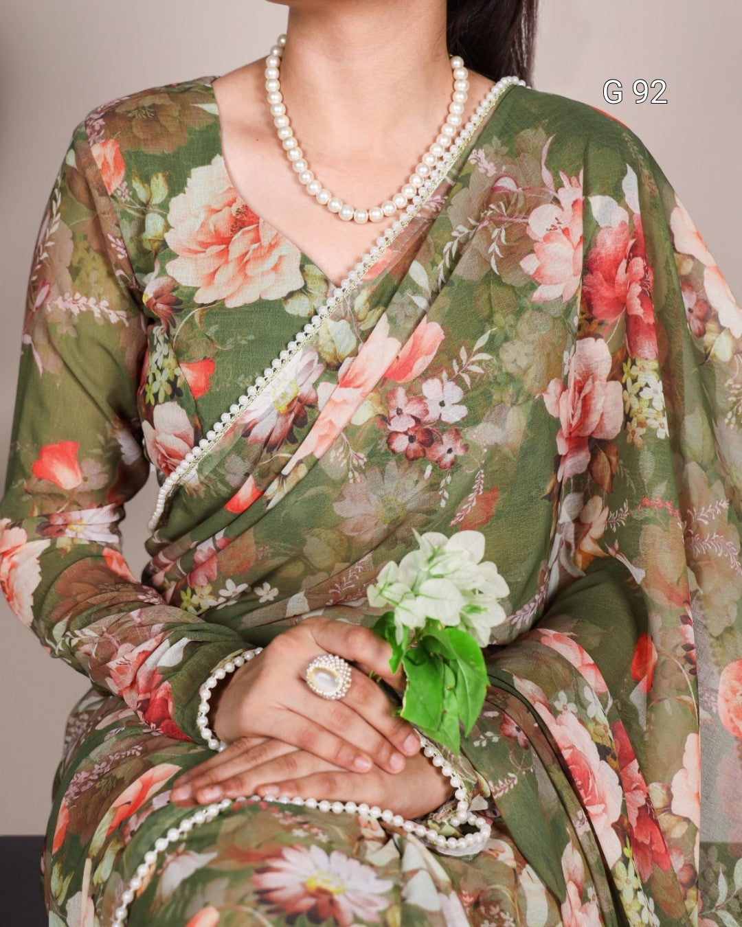 Woman wearing a floral saree with a pearl necklace and ring, holding a white flower.