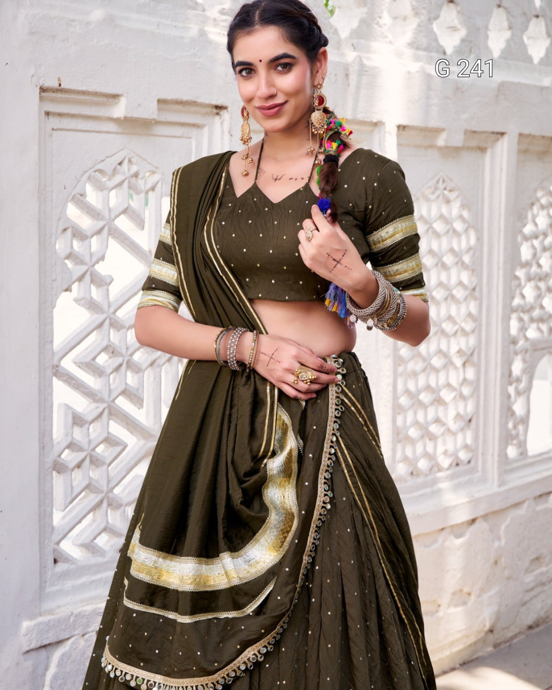 Woman wearing a traditional green saree with gold accents against a white decorative wall.