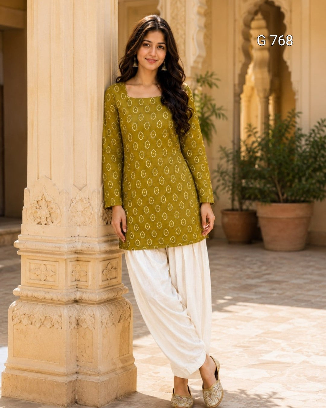 Woman in a green patterned top and white pants standing in front of a stone column.