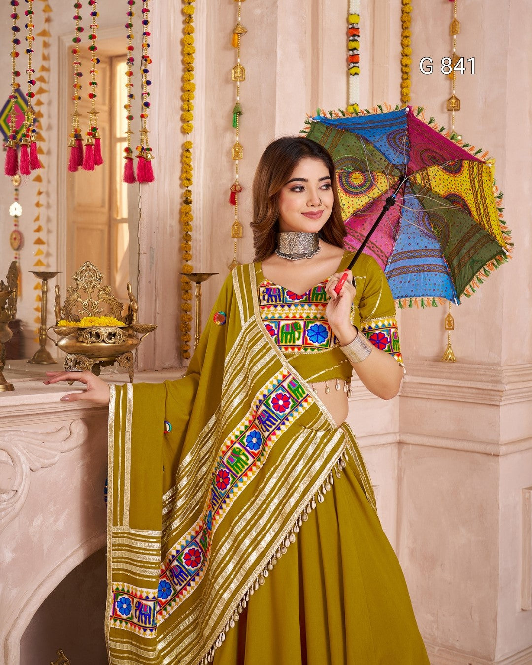 Woman in a traditional outfit holding a colorful umbrella in a decorated interior setting